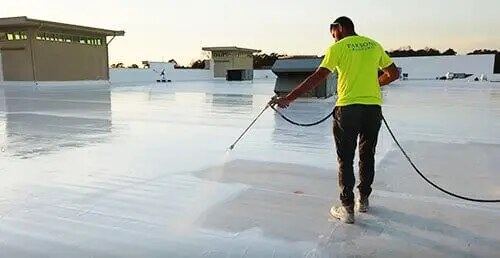 Crew applying a silicone roof coating on a commercial building