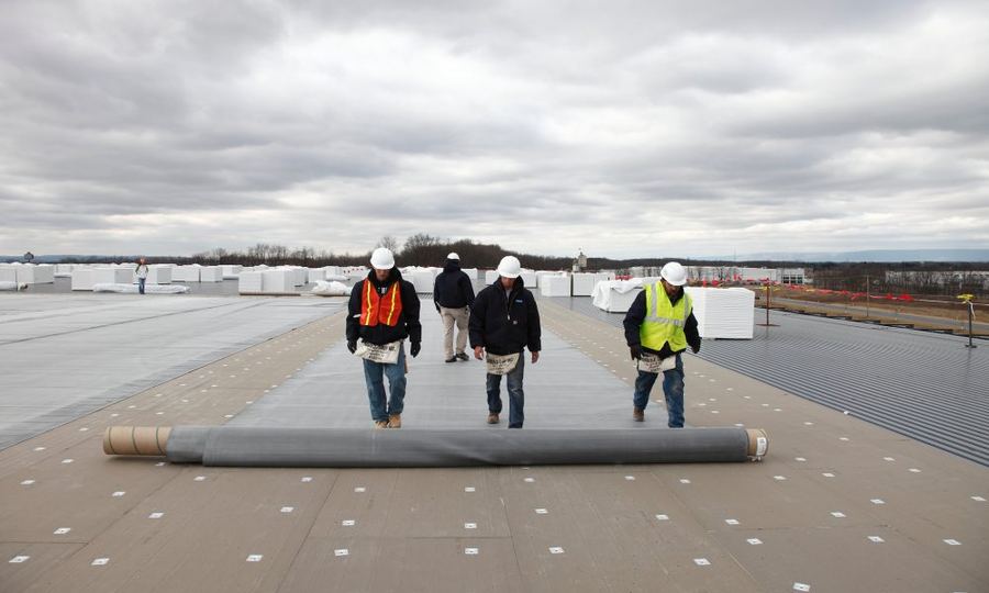 Crew carrying roof insulation board across a large commercial roof deck