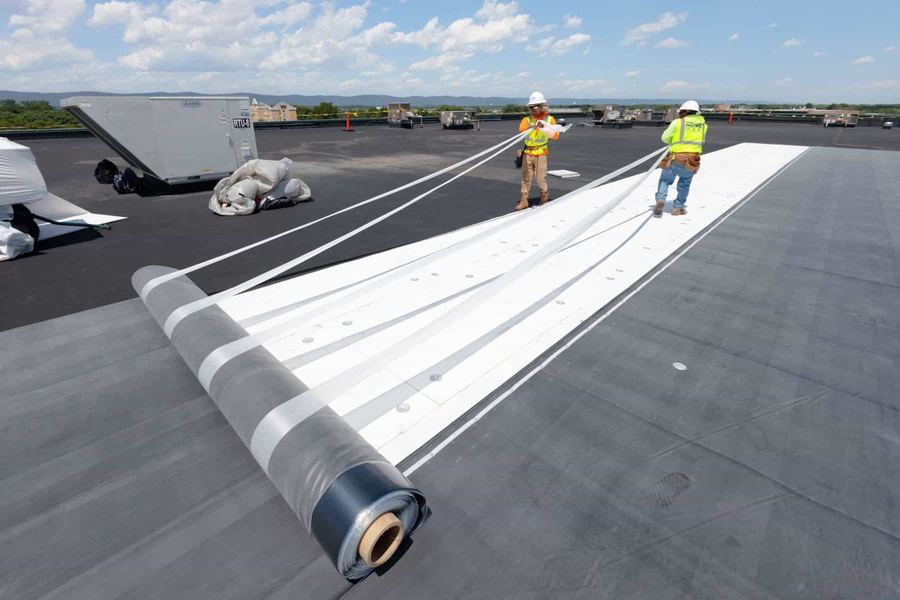 Roofing crew positioning a TPO membrane roll for installation