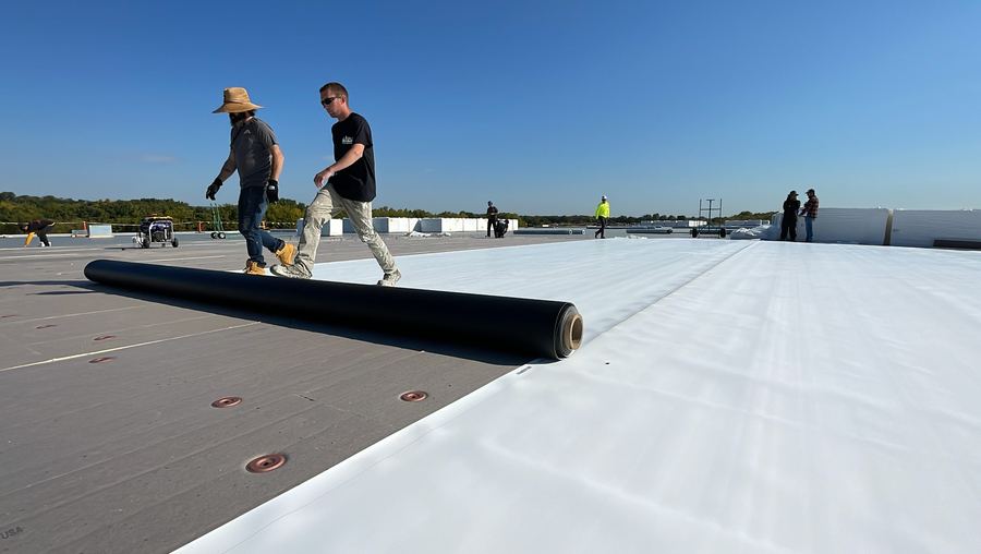 Crew rolling out a white TPO membrane on a large commercial roof